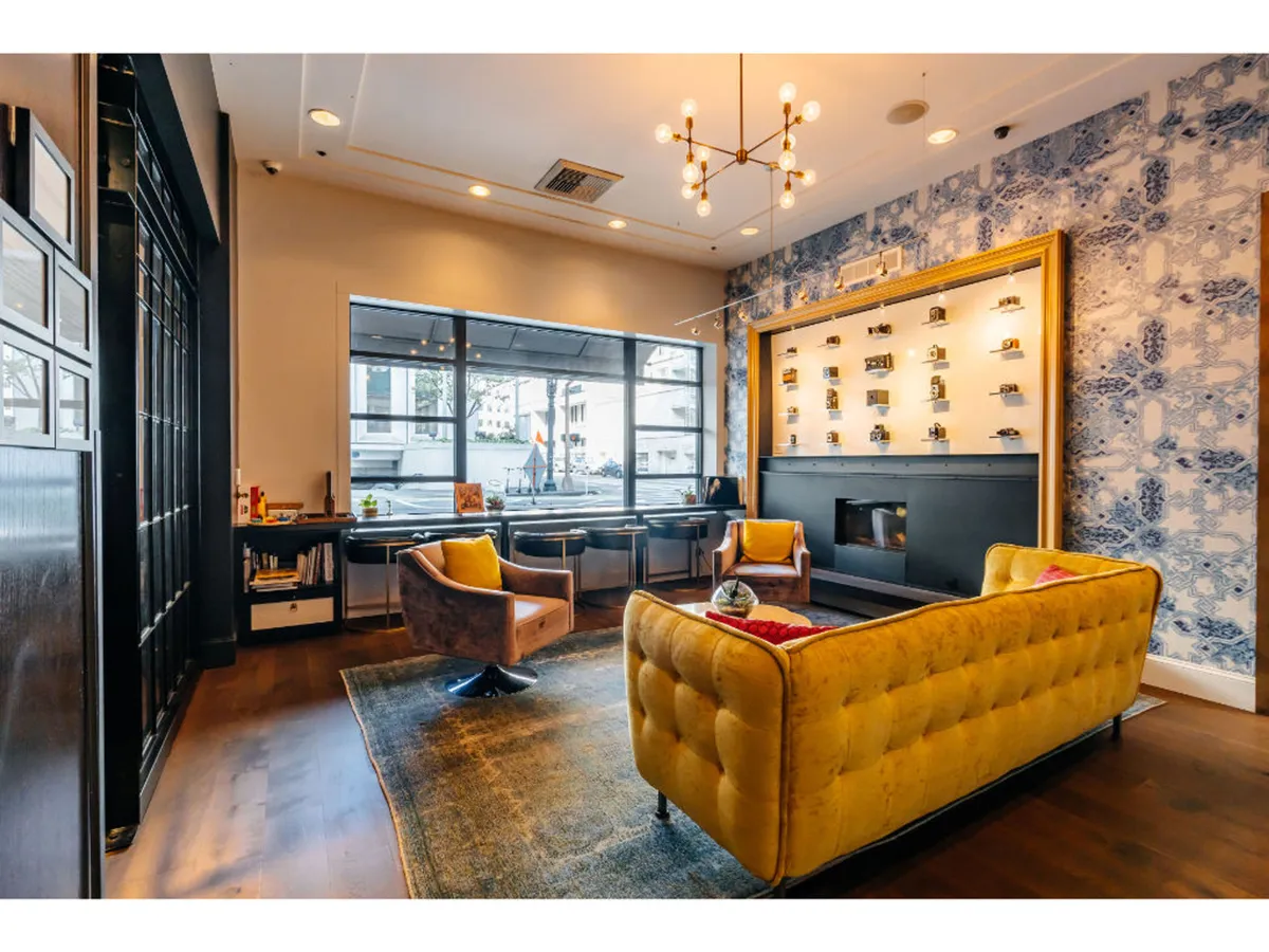 A bright, inviting lounge with a yellow tufted sofa, charming armchairs, and a decorative wall featuring shelves and artistic displays. The atmosphere is cozy, stylish, and perfect for relaxed socializing or unwinding with a book after a day of city adventures.