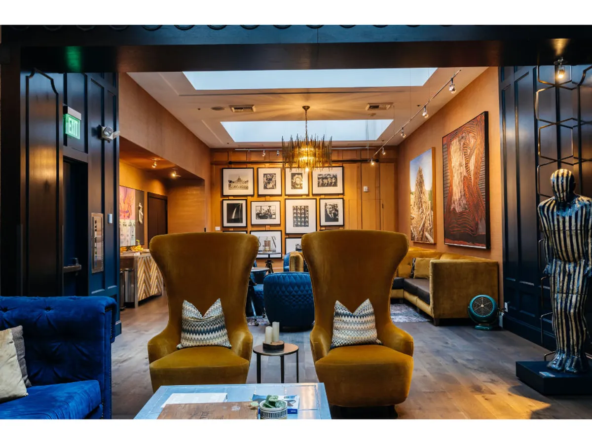 A vibrant interior lounge featuring two large yellow armchairs and a blue sofa, surrounded by striking artwork on the walls and illuminated by a decorative chandelier. The seating arrangement encourages social gatherings and art appreciation in a creative, comfortable setting.