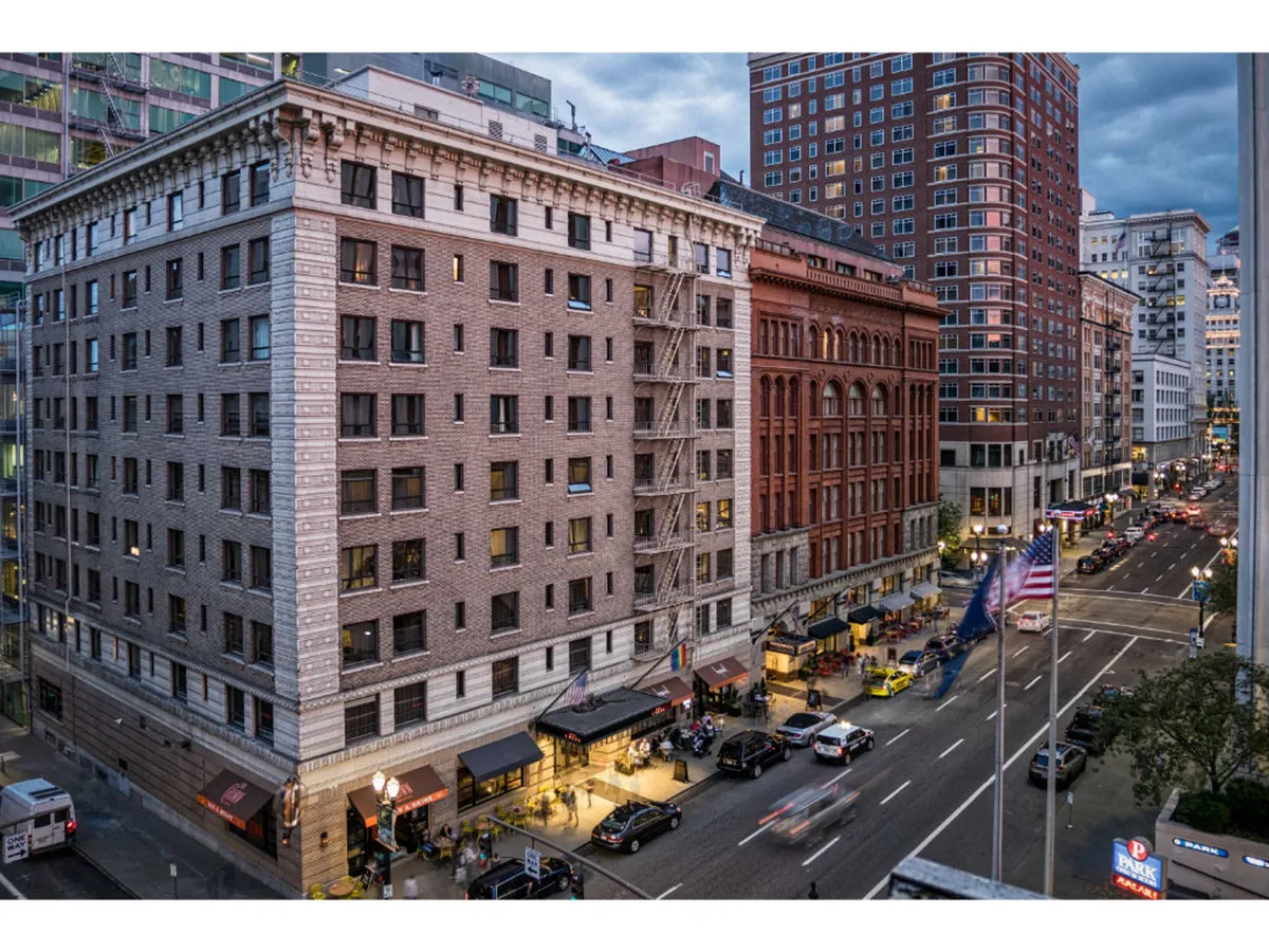 A bustling city street scene featuring historic buildings, outdoor dining areas, and the lively city skyline. People are seen socializing and enjoying the urban atmosphere, showcasing the energy and diversity of downtown Portland’s arts and dining scene.