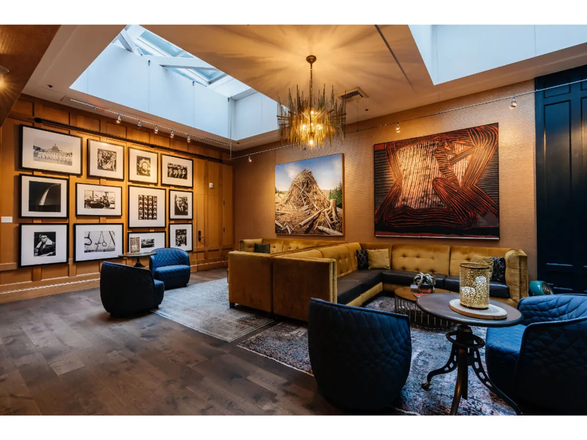 A stylish interior space with large, eye-catching art pieces on the walls, a central seating arrangement, and a distinctive decorative lighting fixture. The atmosphere is both creative and welcoming, designed for art viewing, social gatherings, and relaxation.