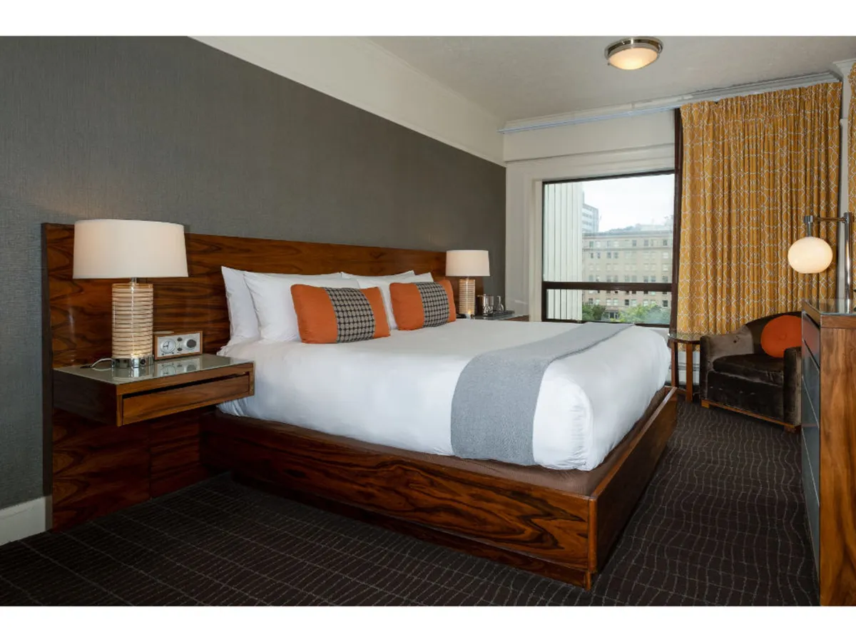 A cozy Superior King room showcasing a luxurious bed, an armchair beside the window, and soft curtains that hint at the city view beyond. The overall mood is warm, comfortable, and quiet—perfect for unwinding.