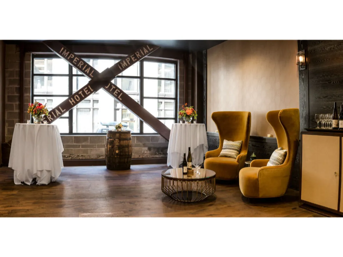 A pair of inviting yellow armchairs paired with white tables and fresh floral arrangements, set beside a rustic wooden barrel and a round coffee table. The scene suggests a welcoming spot for socializing, unwinding, or enjoying curated extras like coffee service or board games.
